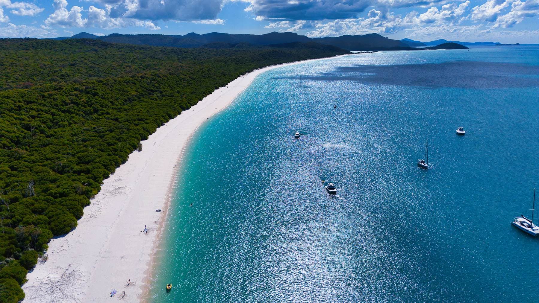 Sailboats anchored in turquoise shallows beside a white-sand beach